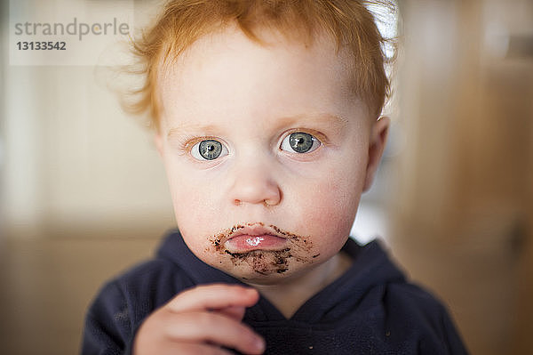 Portrait eines traurigen kleinen Jungen  dem zu Hause Essen um den Mund herumgeworfen wird