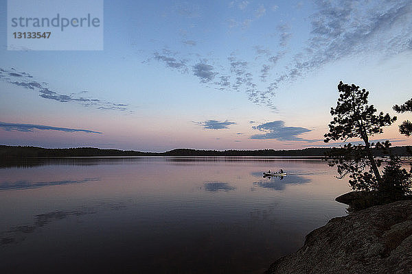 Menschen  die bei Sonnenuntergang in einem Boot auf einem ruhigen See gegen den Himmel fahren