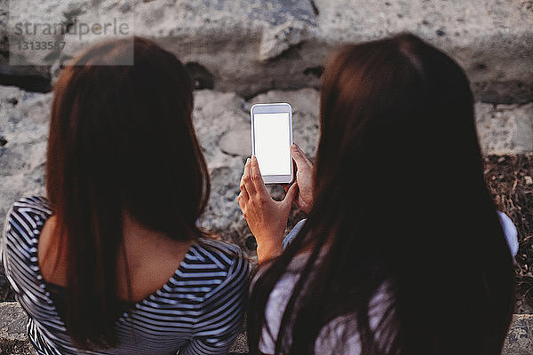 Hochwinkelansicht von Freundinnen  die ein Smartphone im Freien benutzen