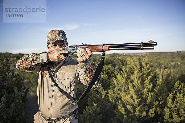 Jäger  der mit dem Gewehr zielt  während er gegen den Himmel steht