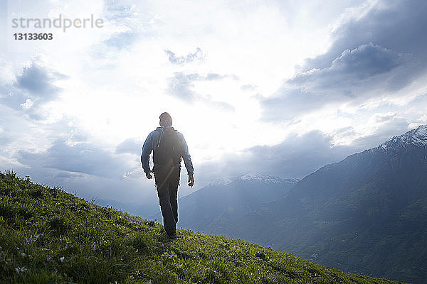 Rückansicht eines männlichen Wanderers  der auf einem Berg vor bewölktem Himmel wandert