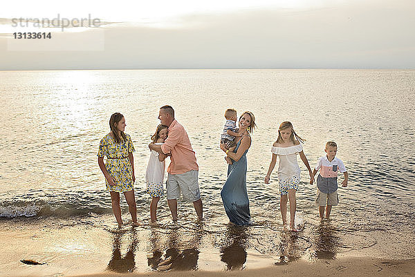Glückliche Familie steht bei Sonnenuntergang gemeinsam am Strand am Ufer