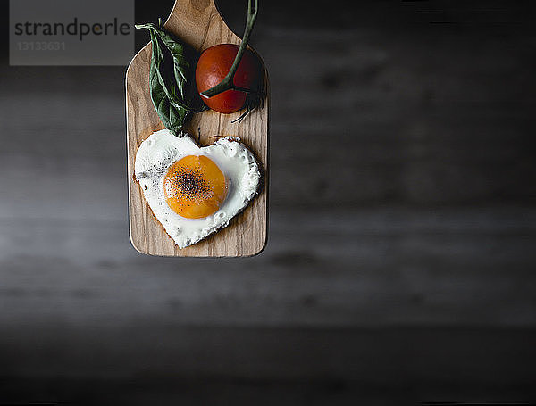 Herzförmiges Sonnenseite-oben-Ei und Tomate auf Schneidebrett