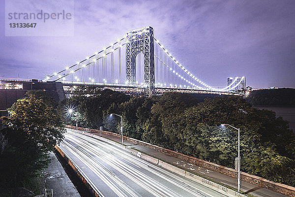 Beleuchtete George-Washington-Brücke über Lichtspuren auf der Straße gegen den Himmel in der Dämmerung