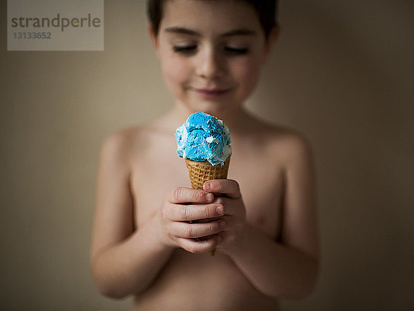 Junge ohne Hemd hält Eiscreme  während er zu Hause an der Wand steht