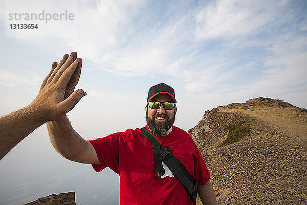 Abgehackte Hand eines Mannes  der einem Freund in den Bergen bei bewölktem Himmel ein High Five gibt