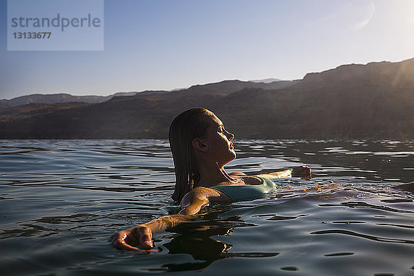 Frau schwimmt bei Sonnenuntergang im Meer gegen klaren Himmel