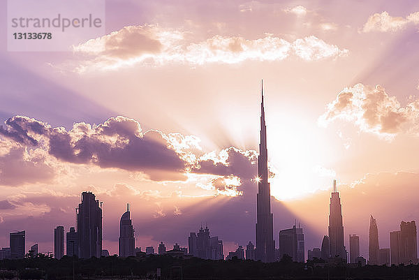 Silhouette des Burj Khalifa und Wolkenkratzer vor bewölktem Himmel bei Sonnenuntergang