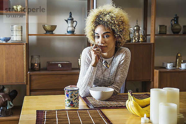 Porträt einer selbstbewussten Frau  die den Löffel hält  während sie im Haus am Tisch sitzt