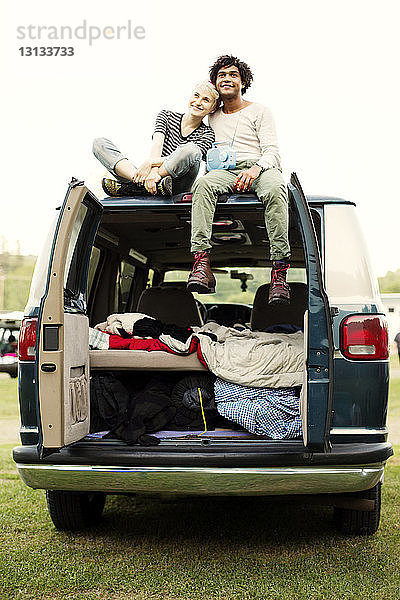 Lächelndes Paar sitzt auf der Motorhaube eines Campingwagens vor klarem Himmel