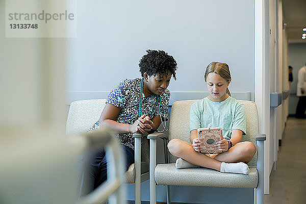 Kinderarzt betrachtet Mädchen mit Tablet-Computer im Krankenhaus