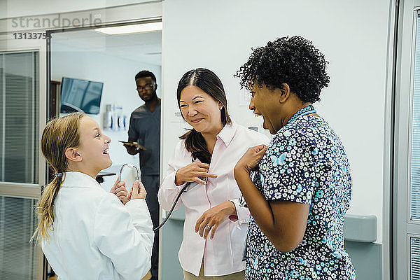 Verspieltes Mädchen schaut die Ärztin an  während sie das Stethoskop beim Kinderarzt im Krankenhauskorridor benutzt