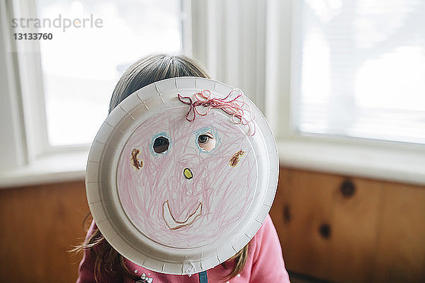 Verspieltes Mädchen schaut mit Teller-Maske weg