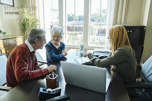Finanzberater erklärt dem älteren Ehepaar den Plan am Tablet-Computer  während es im Büro sitzt
