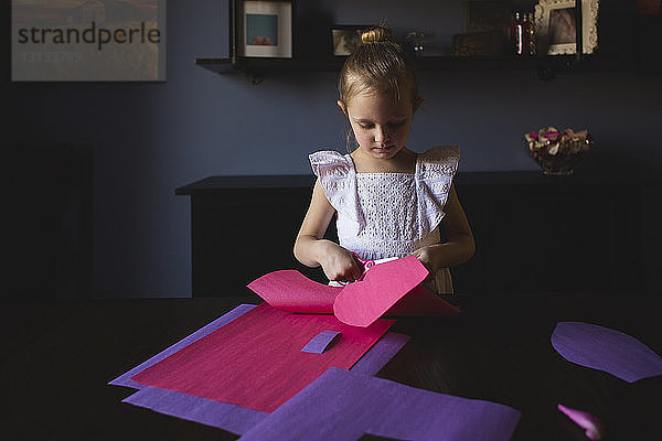 Mädchen schneidet zu Hause Bastelpapier auf dem Tisch