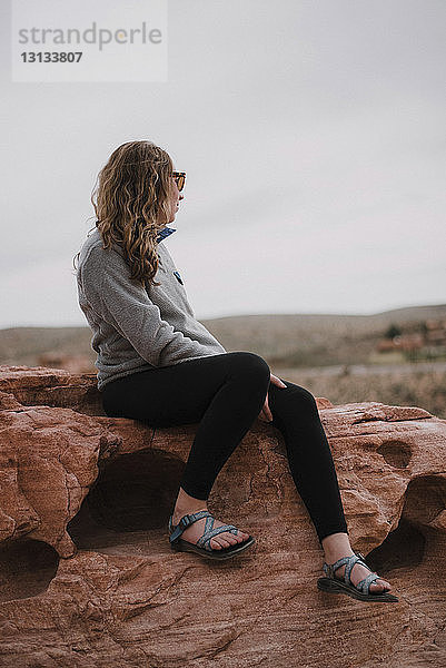 Frau in voller Länge sitzt auf Felsen gegen den Himmel in der Red Rock Canyon National Conservation Area