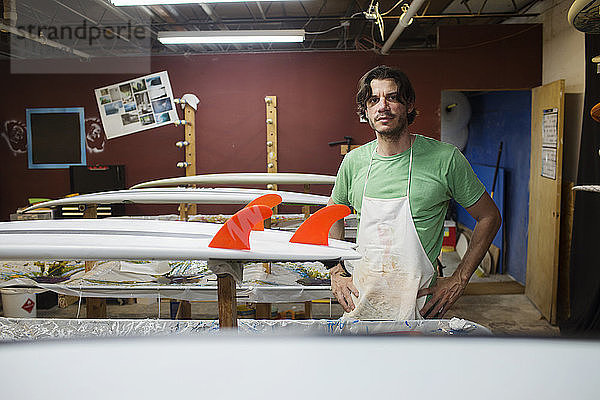 Porträt eines selbstbewussten Arbeiters  der im Workshop an Surfbrettern steht