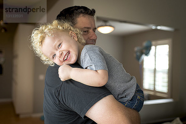 Porträt eines lächelnden Sohnes  der vom Vater zu Hause getragen wird