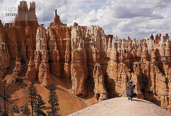 Mann fotografiert Hoodoos  während er auf einem Felsen kauert