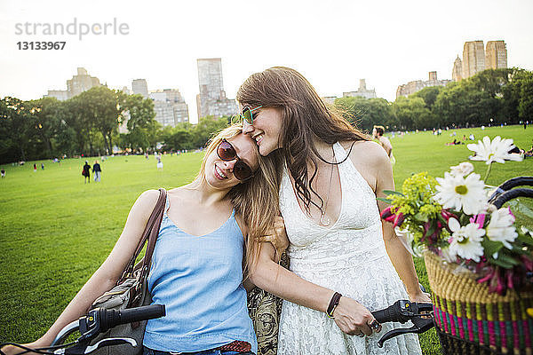 Lächelndes romantisches Lesbenpaar mit Fahrrädern auf Grasfeld im Park