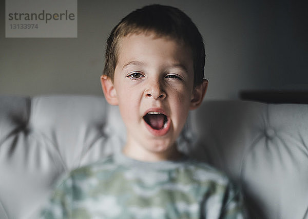 Porträt eines Jungen  der gähnt  während er zu Hause auf dem Bett sitzt