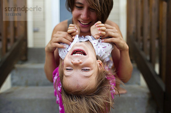 Fröhliche Mutter spielt mit der Tochter  während sie auf Stufen sitzt