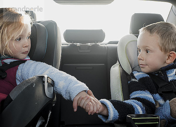 Geschwister  die im Auto sitzen und dabei Händchen halten