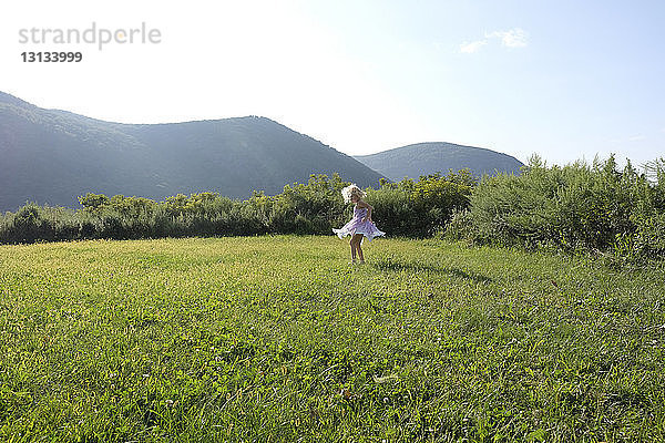 Verspieltes Mädchen  das sich auf einem Grasfeld gegen Berge und Himmel dreht