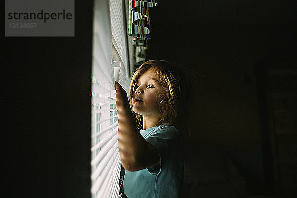 Mädchen schaut durch Fensterläden  während sie zu Hause in der Dunkelkammer steht