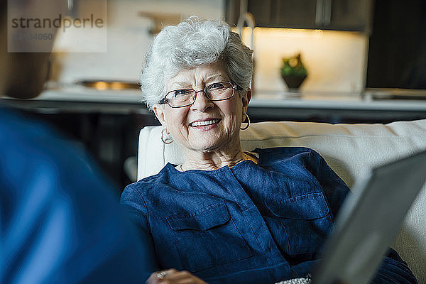 Glückliche ältere Frau schaut im Wohnzimmer auf die häusliche Pflegekraft