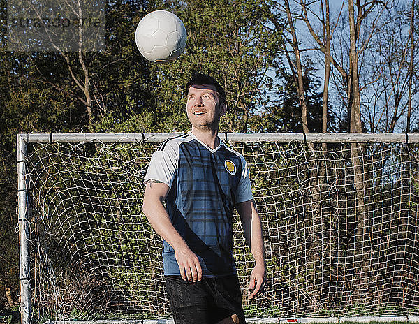 Glücklicher Mann spielt mit Fussball gegen Bäume im Park