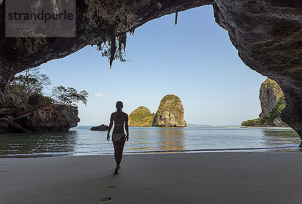 Rückansicht einer Frau im Bikini  die am Strand spazieren geht  durch eine Höhle gesehen