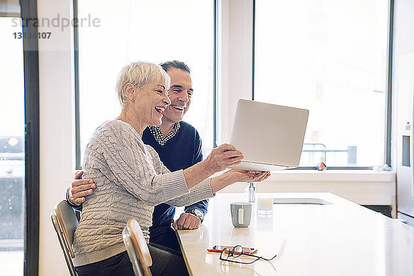Glückliche ältere Frau hält Laptop-Computer  während sie mit einem Mann am Tisch sitzt