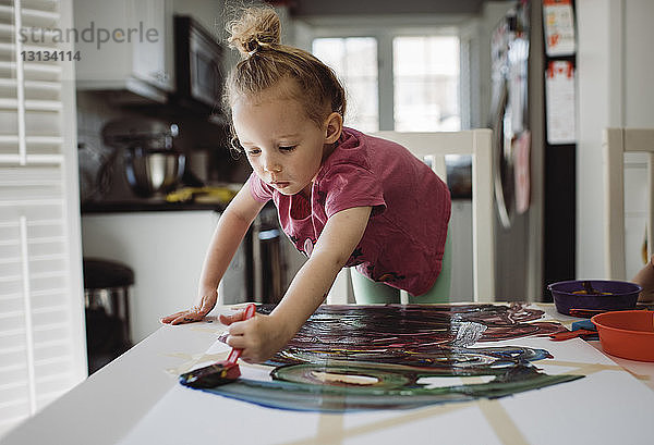 Mädchen malt auf Papier  während sie zu Hause am Tisch steht