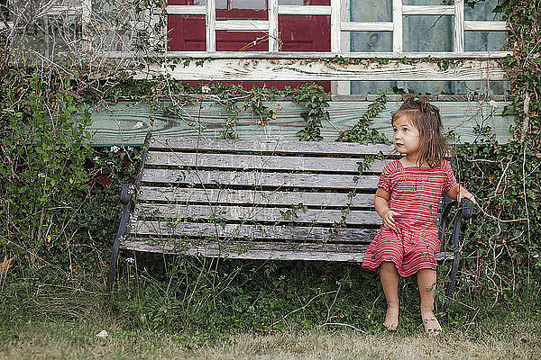 Ein süßes Mädchen in voller Länge sitzt auf einer verlassenen Parkbank