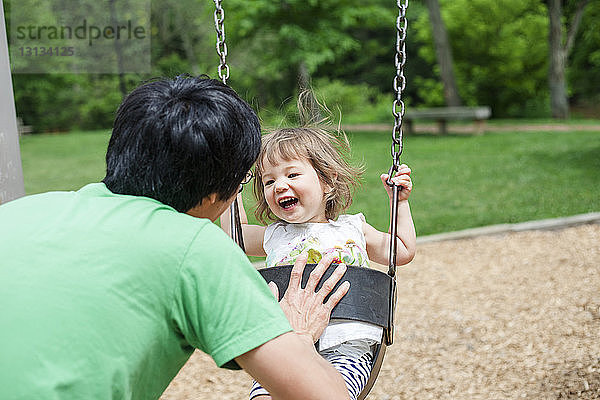 Rückansicht eines Vaters  der seine glückliche Tochter auf dem Spielplatz schubst