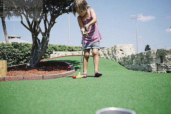Mädchen spielt Minigolf an einem sonnigen Tag