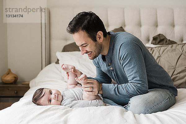 Vater spielt mit dem Sohn  während er zu Hause im Bett sitzt