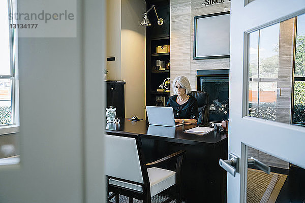 Geschäftsfrau  die am Laptop-Computer am Schreibtisch im Büro arbeitet  durch die Tür gesehen