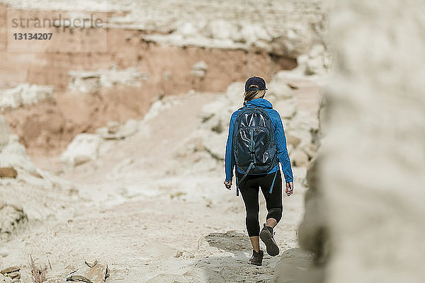 Rückansicht einer Wanderin mit Rucksack beim Wandern gegen Felsformationen in der Wüste