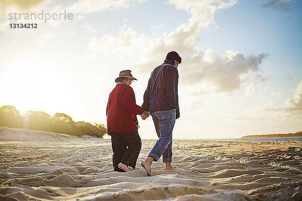 Älteres Ehepaar hält an sonnigen Tagen beim Spaziergang am Sandstrand Händchen