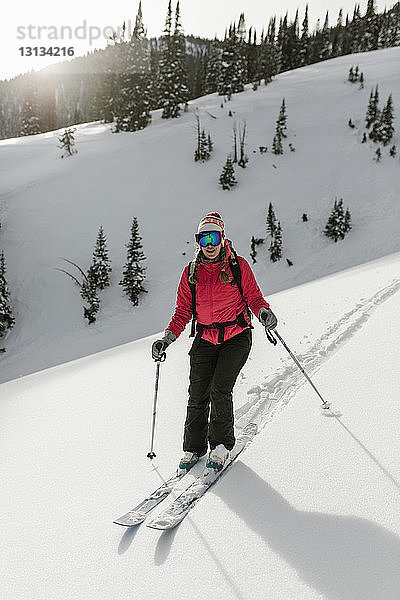 Frau fährt Ski auf schneebedecktem Berg im Wald