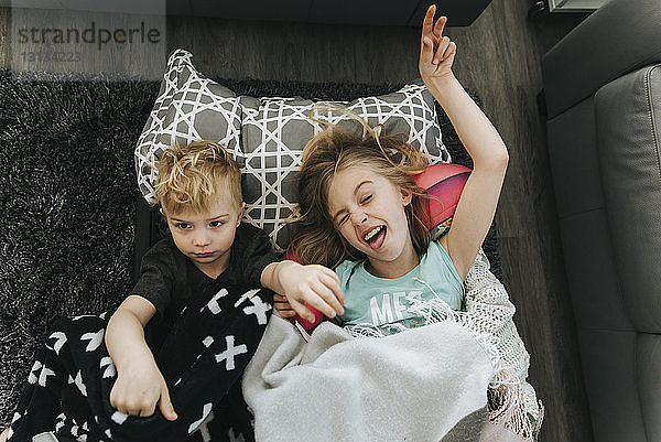 Schrägansicht auf glückliche Geschwister  die sich zu Hause auf dem Teppich entspannen