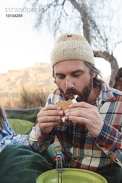 Mittelgroßer erwachsener Mann isst s'more auf dem Campingplatz