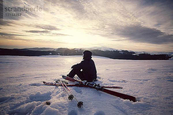 Rückansicht eines auf einem verschneiten Berg sitzenden Skifahrers gegen den Himmel