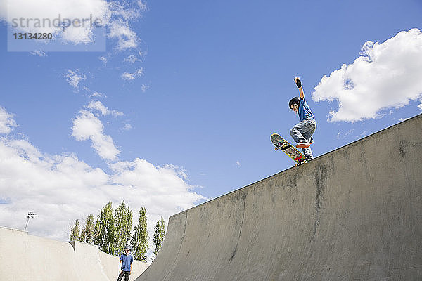 Niedrigwinkel-Ansicht eines Skateboard fahrenden Jungen auf der Rampe vor blauem Himmel
