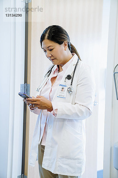 Ärztin benutzt Smartphone  während sie im Krankenhaus gegen die Tür steht