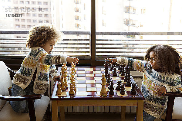 Schwestern spielen zu Hause am Tisch gegen das Fenster Schach