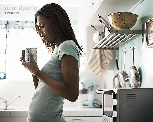 Lächelnde Frau hält Kaffeetasse  während sie an der Küchentheke steht