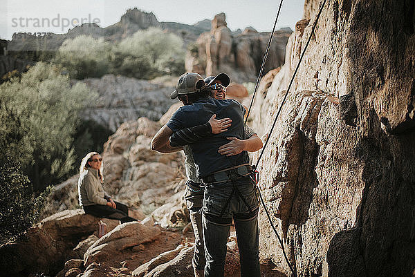 Frau schaut auf männliche Freunde  die eine Felsformation im Red Rock Canyon National Conservation Area umarmen